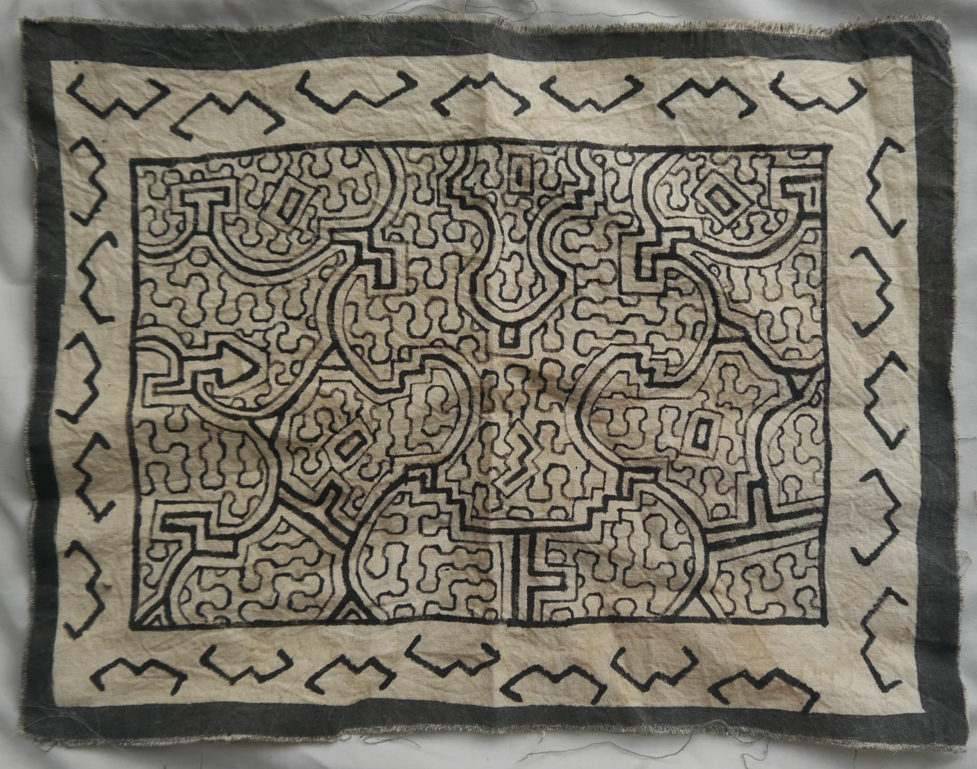 Black geometric kené lines and branching motifs on a cream Shipibo textile